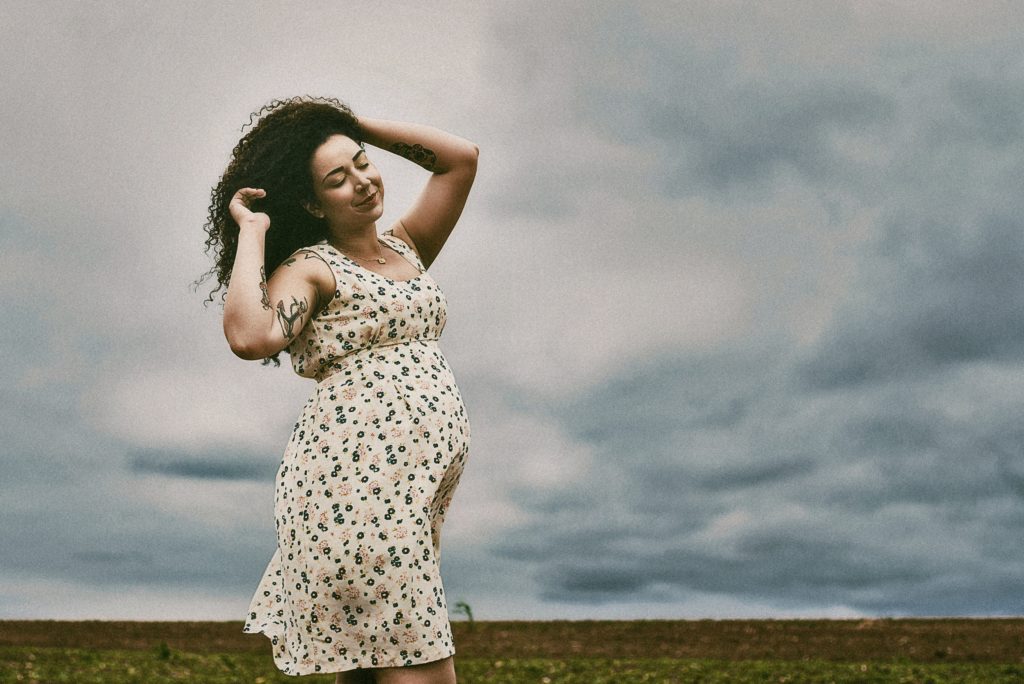 Adult in flowered dress with tattoos walking with eyes closed and hands in long hair